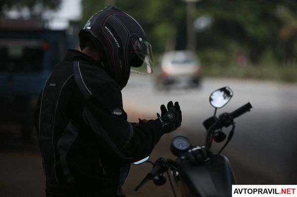 Мотоциклист в шлеме, застегивающий перчатку